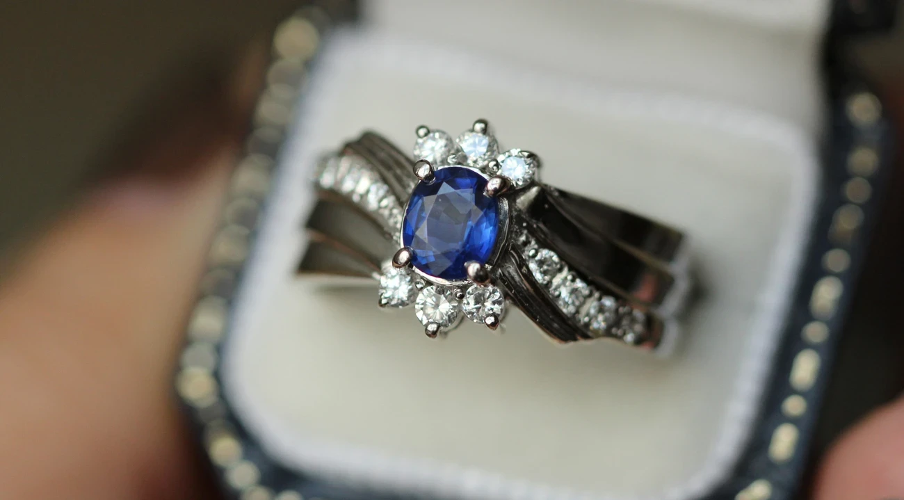 An exquisite, vintage sapphire ring showcasing a deep blue, oval-cut sapphire, elegantly framed by intricate, milgrain detailing, and accented with sparkling white diamonds set in a delicate, yellow gold band. 