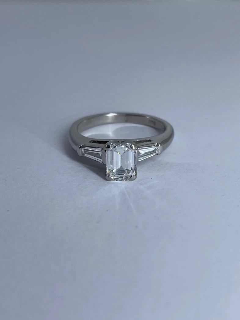 A stunning emerald-cut diamond engagement ring showcased on a delicate band, glistening with precision-cut facets. 