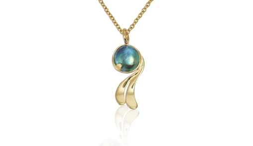 A stunning Pacific blue pearl pendant set in a delicate silver mount, reflecting the subtle hues of the ocean, showcased against a beige background. 
