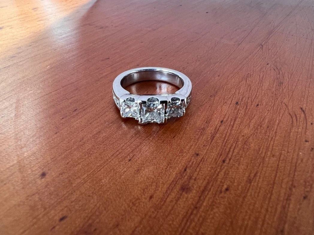 A beautifully crafted platinum three-stone ring featuring a central diamond flanked by two smaller diamonds, elegantly set in a streamlined and sophisticated mount. 