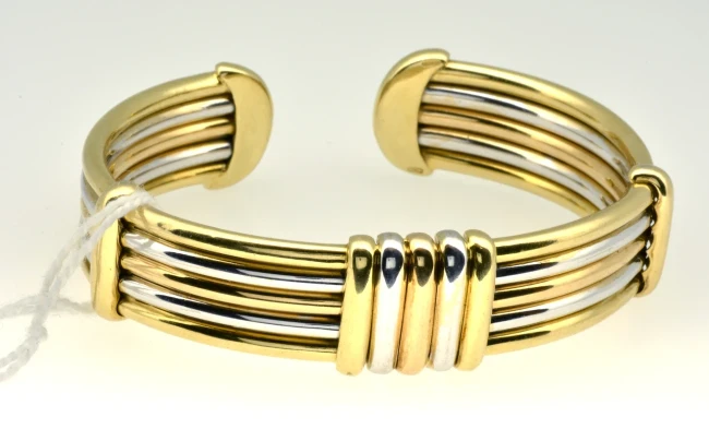 An elegant 18-carat gold snap bangle, characterised by its sleek design and polished finish, is captured in close-up against a neutral background. 