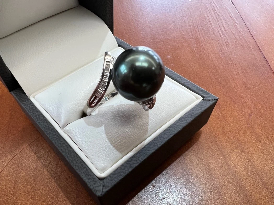 A captivating 18ct white gold ring featuring a large black pearl at its centre, surrounded by a delicate arrangement of sparkling diamonds that accentuate its elegance and sophistication.